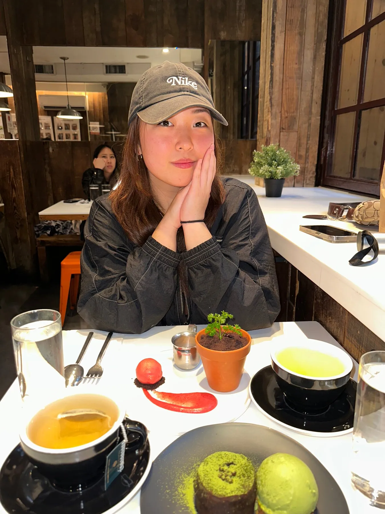 Christine in a grey cap, chin resting on her hands at a café table.