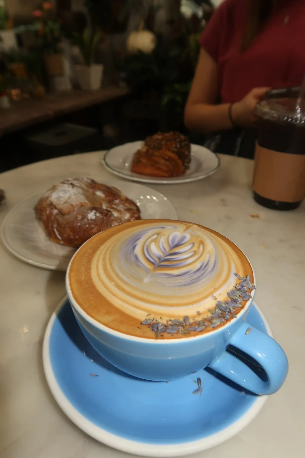 A latte with purple and gold latte art in a blue cup, pastries behind it.
