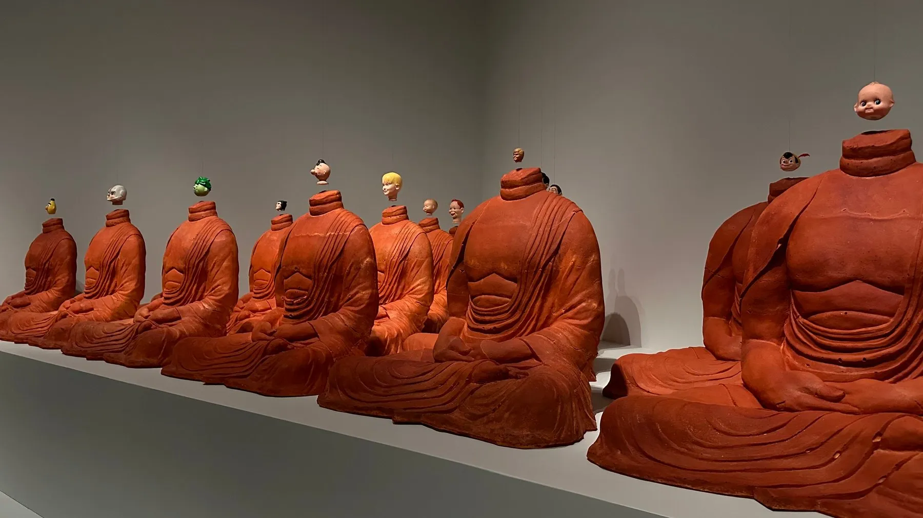 A row of small terracotta seated figures on a gallery shelf.