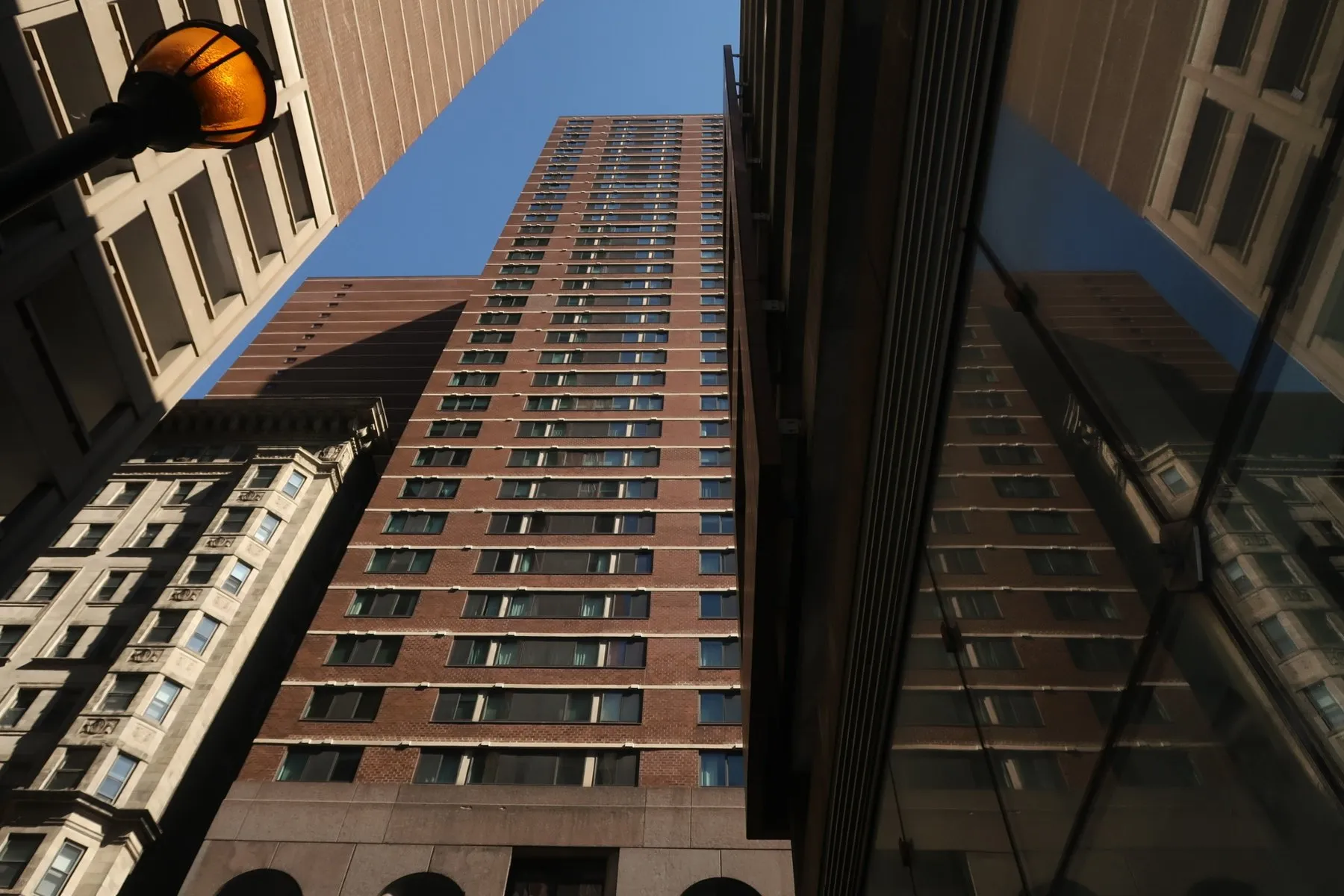 Looking up at a brick tower between two buildings against a blue sky.