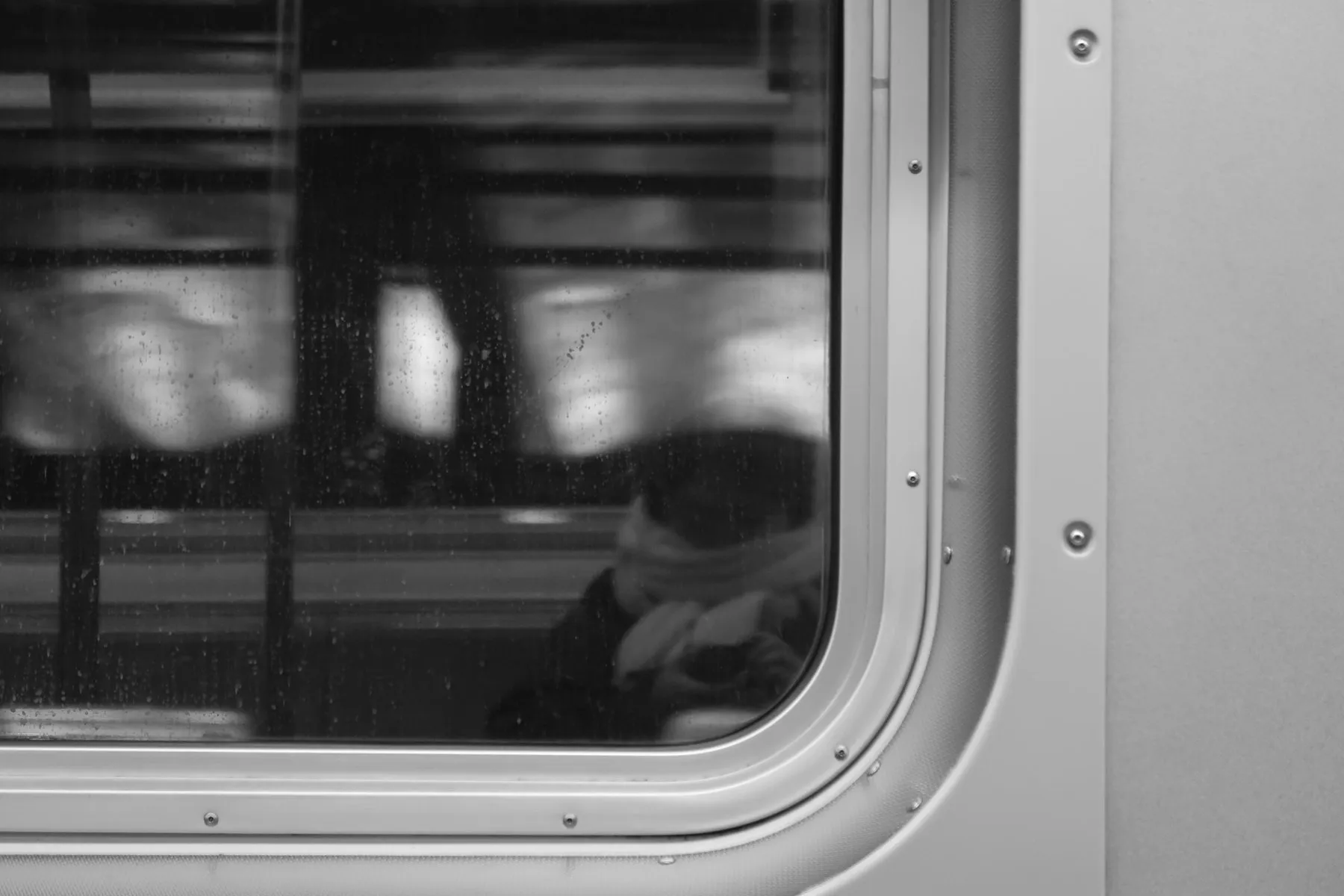Black and white photo of a train window with blurred lights passing outside.