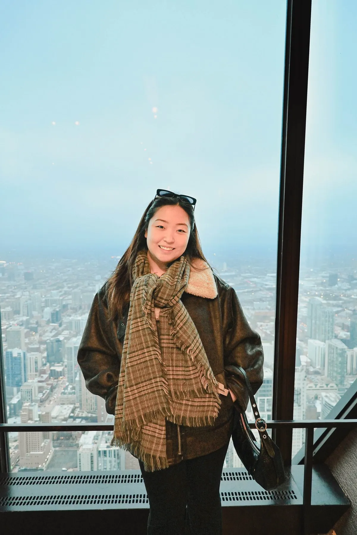 Christine smiling in front of a floor-to-ceiling window high above a city.